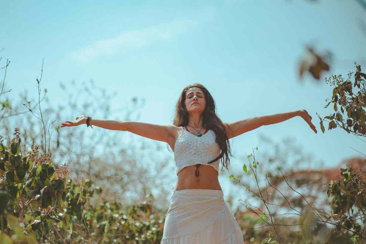 Una ragazza con le braccia aperte e gli occhi chiusi in mezzo alla natura