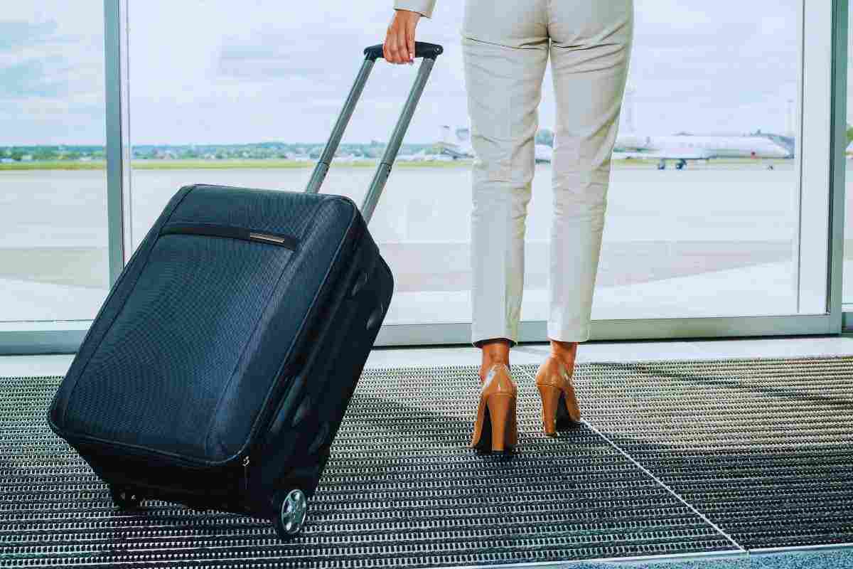 Le gambe di una donna con accanto il suo trolley